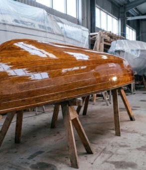 Frisch mit Bootslack lackiertes Holzboot kieloben auf Boecken in der Werfthalle, tiefglaenzende Oberflaeche